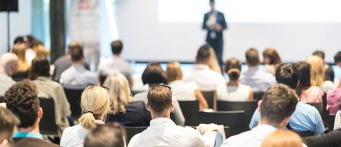 Speaker giving a talk in conference hall at business event. Audience at the conference hall. Business and Entrepreneurship concept. Focus on unrecognizable people in audience.