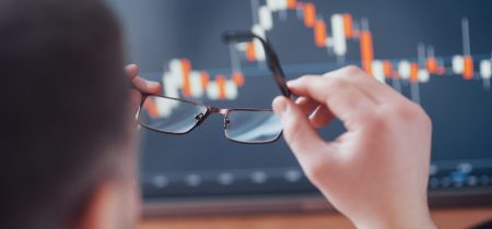Analyzing data. Close up of a young businessman who holds glasses and looks at the gff while working in a creative office.