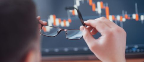 Analyzing data. Close up of a young businessman who holds glasses and looks at the gff while working in a creative office.