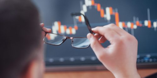 Analyzing data. Close up of a young businessman who holds glasses and looks at the gff while working in a creative office.