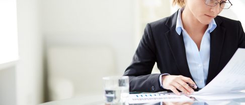 Young businesswoman sitting at workplace and reading paper in office